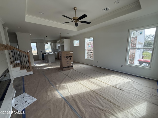 unfurnished living room featuring visible vents, stairway, a tray ceiling, and ornamental molding