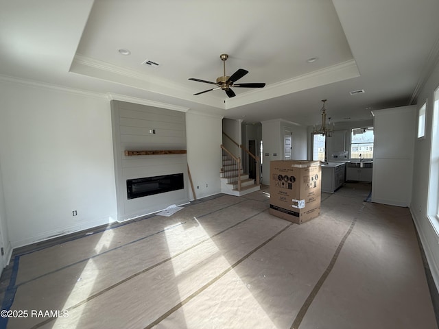 unfurnished living room with a glass covered fireplace, a tray ceiling, visible vents, and ornamental molding