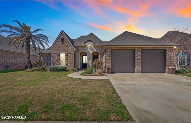 french country style house featuring driveway, a garage, a front lawn, and brick siding