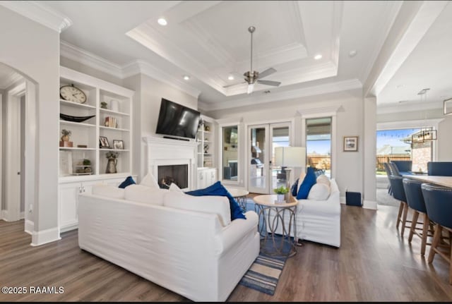 living area featuring dark wood-style floors, a fireplace, a tray ceiling, and crown molding