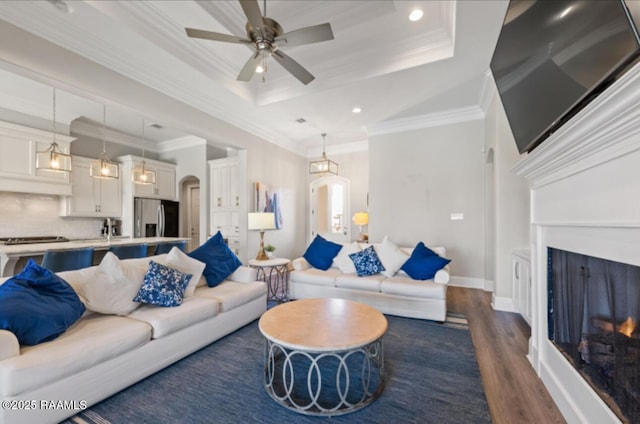 living area featuring ornamental molding, a raised ceiling, dark wood finished floors, and a lit fireplace