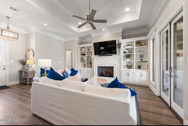 living area with arched walkways, a tray ceiling, dark wood-type flooring, and crown molding