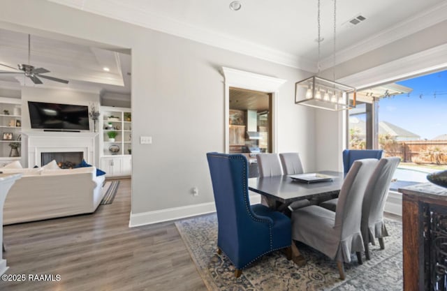 dining room with a fireplace, wood finished floors, visible vents, baseboards, and ornamental molding