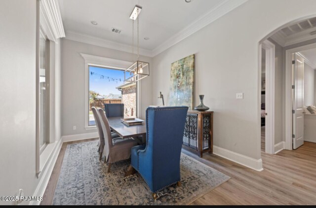 dining area with arched walkways, baseboards, wood finished floors, and crown molding