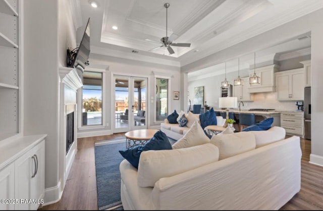 living room featuring a tray ceiling, ornamental molding, dark wood finished floors, and french doors