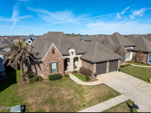 french provincial home featuring brick siding, roof with shingles, concrete driveway, an attached garage, and a front yard