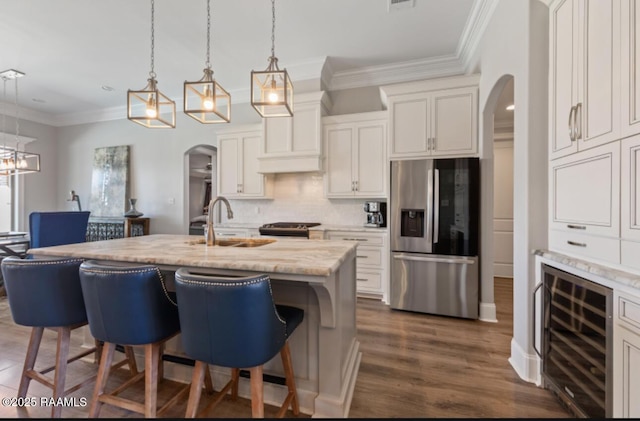 kitchen with tasteful backsplash, beverage cooler, arched walkways, appliances with stainless steel finishes, and a kitchen breakfast bar