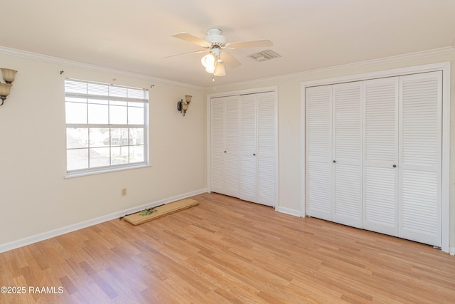 unfurnished bedroom featuring light wood-type flooring, baseboards, ornamental molding, and two closets