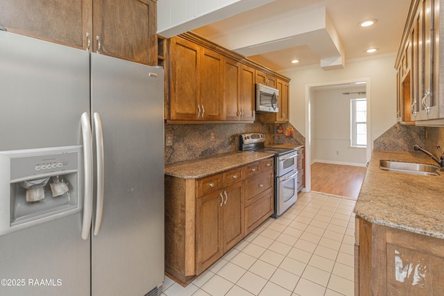 kitchen with stainless steel appliances, brown cabinetry, a sink, and tasteful backsplash