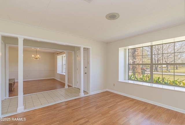 unfurnished room with light wood-type flooring, ornate columns, a notable chandelier, and baseboards