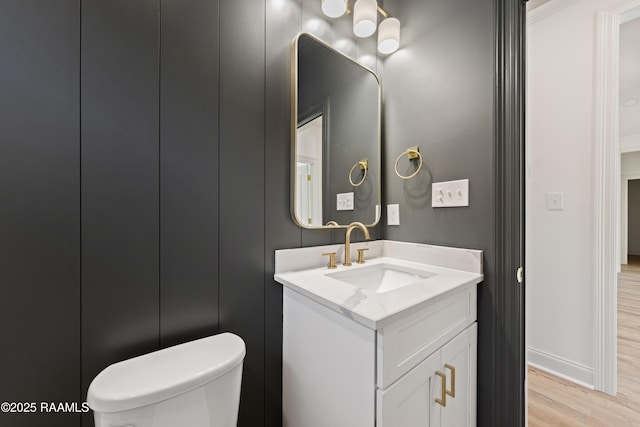 half bathroom with toilet, baseboards, wood finished floors, and vanity