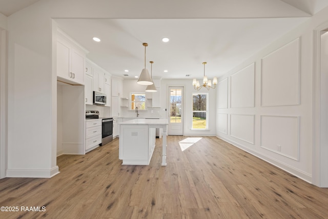 kitchen with light countertops, a decorative wall, appliances with stainless steel finishes, white cabinetry, and light wood-type flooring