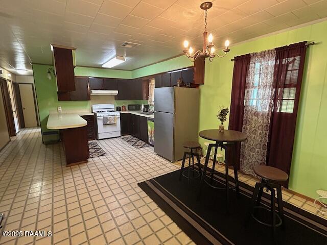 kitchen with light countertops, freestanding refrigerator, a peninsula, under cabinet range hood, and white gas range oven