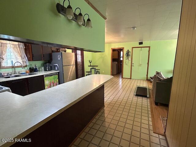 kitchen featuring light countertops, freestanding refrigerator, dark brown cabinetry, a sink, and dishwashing machine