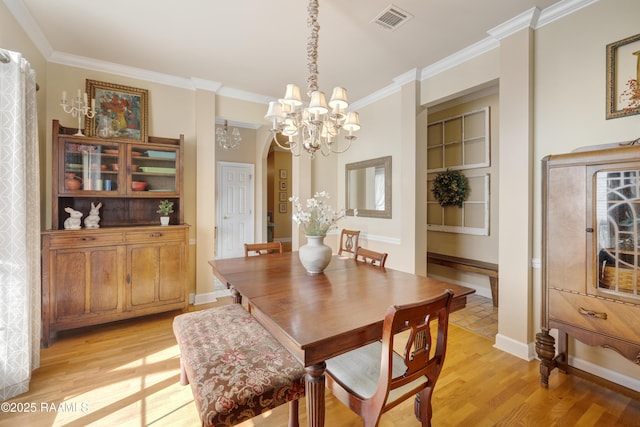 dining area with visible vents, an inviting chandelier, light wood-style flooring, and ornamental molding