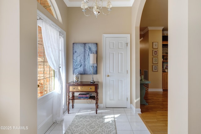 foyer with crown molding, baseboards, a chandelier, light tile patterned floors, and arched walkways