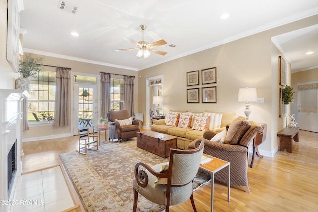 living area featuring visible vents, baseboards, ornamental molding, a fireplace, and light wood-style floors