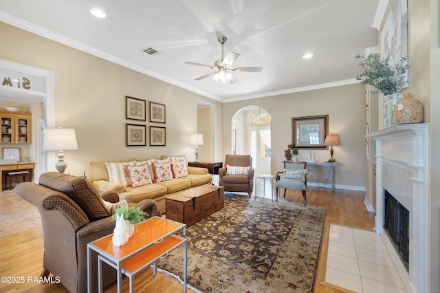 living area featuring visible vents, ceiling fan, crown molding, and a fireplace with flush hearth