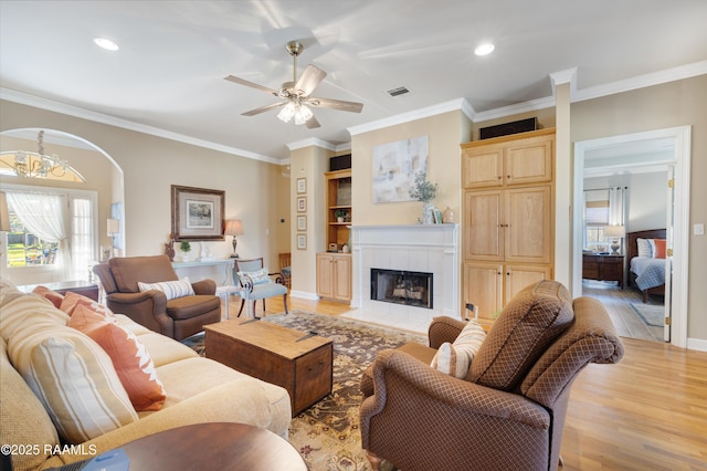 living room with visible vents, light wood-style floors, crown molding, baseboards, and a tile fireplace