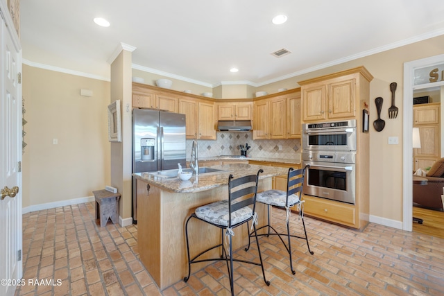 kitchen with baseboards, a sink, light brown cabinetry, appliances with stainless steel finishes, and tasteful backsplash