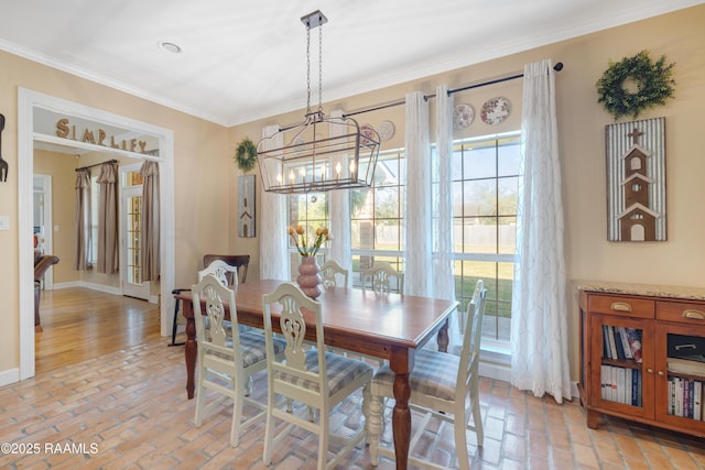 dining space with an inviting chandelier, crown molding, baseboards, and brick floor