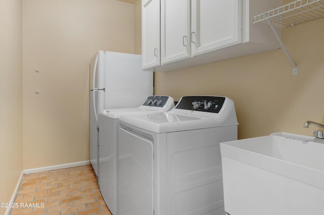 laundry room featuring baseboards, washer and dryer, brick floor, cabinet space, and a sink