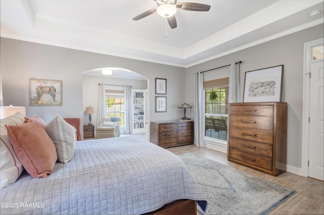 bedroom featuring a tray ceiling, multiple windows, arched walkways, and wood finished floors