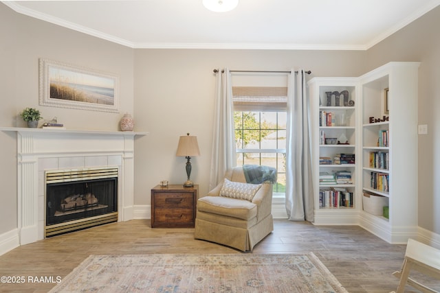 living area featuring a tile fireplace, crown molding, baseboards, and wood finished floors