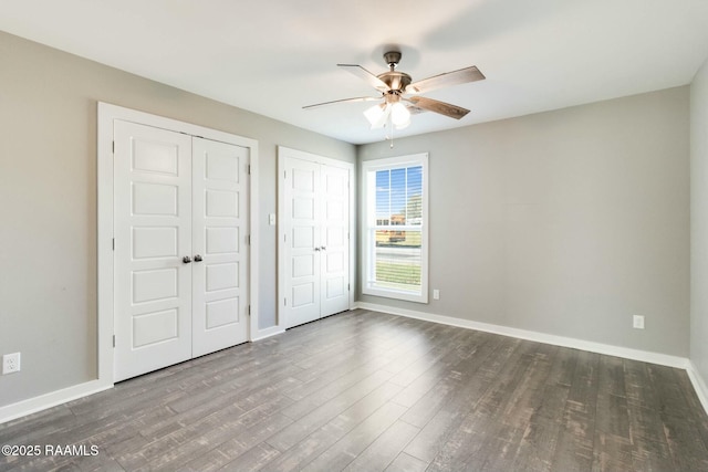 unfurnished bedroom featuring ceiling fan, multiple closets, wood finished floors, and baseboards