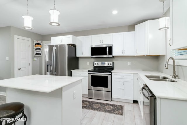 kitchen featuring a kitchen island, appliances with stainless steel finishes, hanging light fixtures, white cabinetry, and a sink