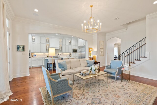 living area featuring light wood finished floors, baseboards, arched walkways, and ornamental molding