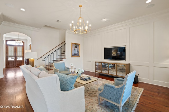 living area with arched walkways, hardwood / wood-style flooring, stairway, crown molding, and a decorative wall