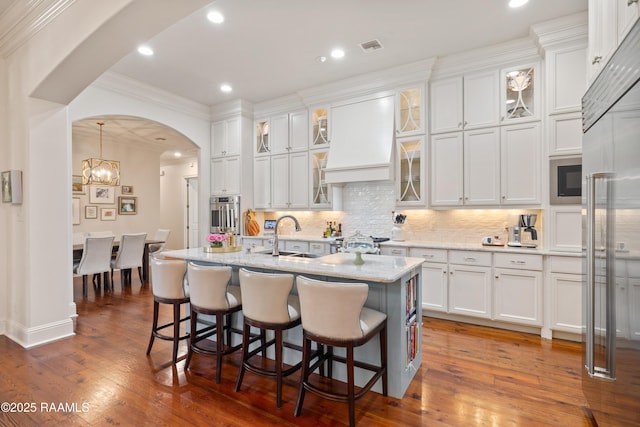 kitchen featuring white cabinetry, custom range hood, arched walkways, and a sink