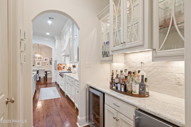 bar featuring arched walkways, dark wood finished floors, tasteful backsplash, visible vents, and beverage cooler