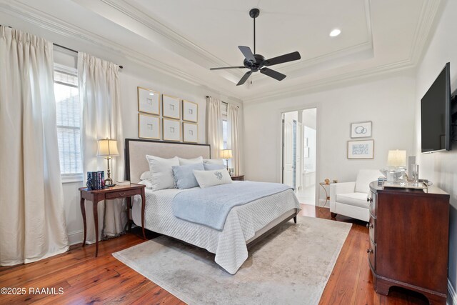 bedroom with a ceiling fan, hardwood / wood-style floors, a tray ceiling, ensuite bath, and crown molding