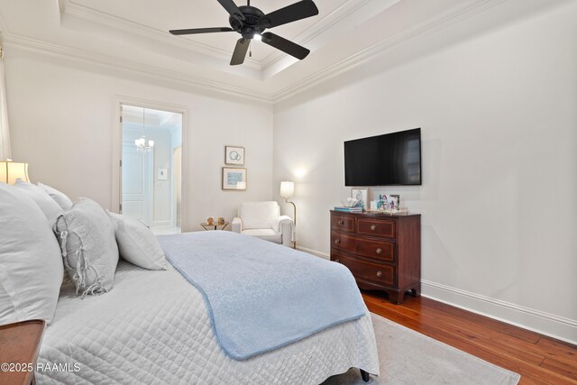 bedroom featuring baseboards, a tray ceiling, wood finished floors, and crown molding