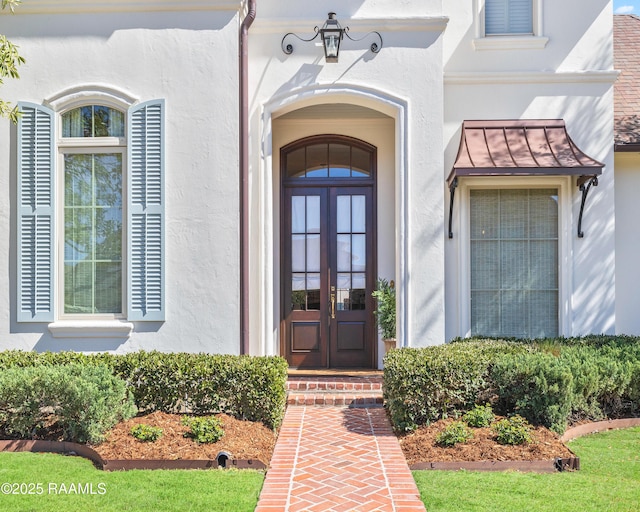 entrance to property with french doors, metal roof, a standing seam roof, and stucco siding