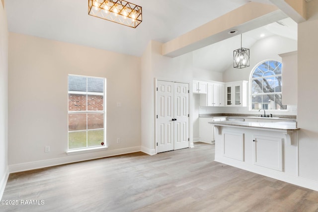 kitchen with light wood finished floors, glass insert cabinets, a healthy amount of sunlight, white cabinets, and a peninsula