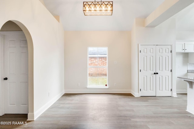 interior space with arched walkways, light wood finished floors, and baseboards