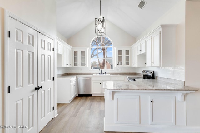 kitchen with light stone counters, a peninsula, a sink, appliances with stainless steel finishes, and glass insert cabinets