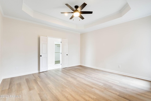 spare room with light wood-style flooring, a raised ceiling, and crown molding