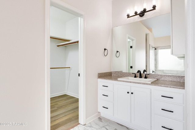 full bath featuring a walk in closet, marble finish floor, vanity, and baseboards