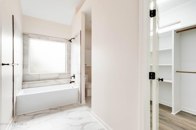 bathroom featuring marble finish floor, baseboards, toilet, and bathtub / shower combination