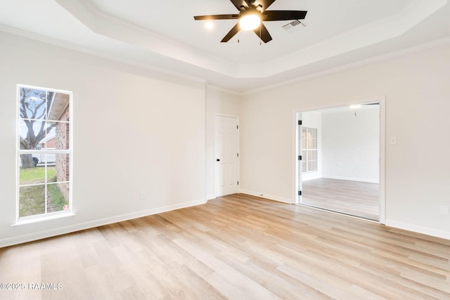 empty room featuring light wood finished floors, visible vents, baseboards, ornamental molding, and a tray ceiling