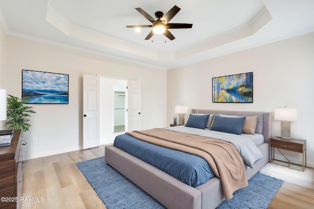 bedroom with light wood-style floors, baseboards, a tray ceiling, and ornamental molding