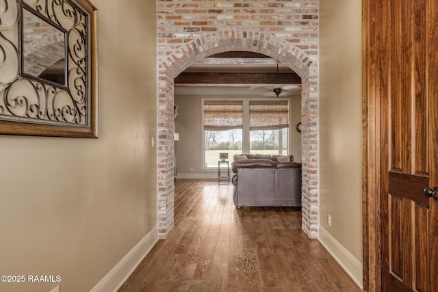 hall with baseboards, arched walkways, dark wood finished floors, and beam ceiling