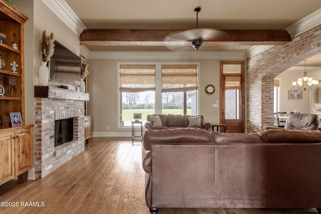 living room featuring arched walkways, wood-type flooring, ornamental molding, a fireplace, and beam ceiling