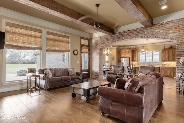 living area featuring arched walkways, ceiling fan with notable chandelier, brick wall, beamed ceiling, and wood-type flooring