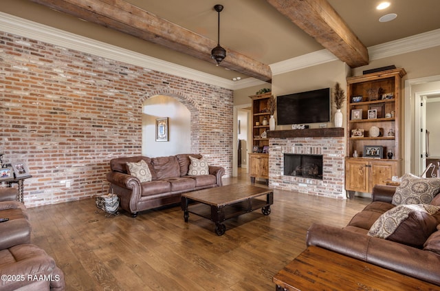 living area featuring beam ceiling, a fireplace, wood-type flooring, and brick wall