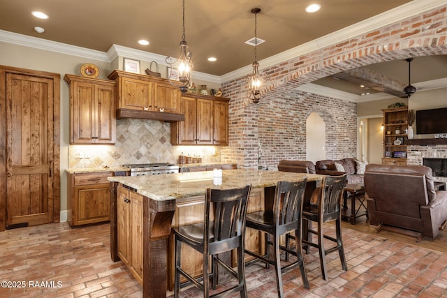 kitchen featuring brick floor, backsplash, stove, brown cabinetry, and open floor plan